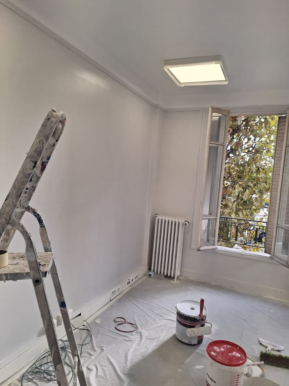 Bureau en fin de chantier : bâche de protection, pots de peinture et escabeau au sol